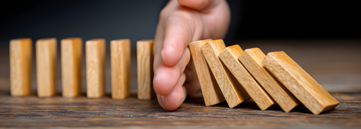 Een hand voorkomt een keting reactie van houten domino steentjes